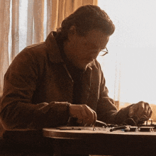 a man wearing glasses sits at a table working on a piece of equipment