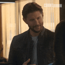 a man in a leather jacket is smiling while talking to a woman