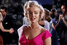 a woman in a pink dress and earrings is standing in front of a crowd of people .