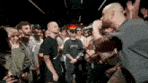 a man wearing a metallica shirt stands in front of a crowd of people