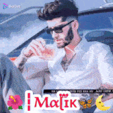 a man with a beard is sitting in a car drinking from a glass with the name malik on it