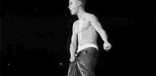 a black and white photo of a shirtless man holding a microphone on stage .