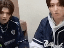 two young men wearing baseball jerseys are sitting next to each other .