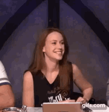 a woman is sitting at a table with a laptop computer and smiling .