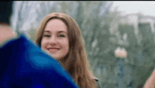 a woman is smiling while holding a blue umbrella in her hand .