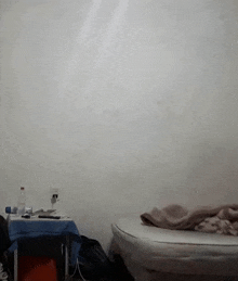 a bed with a blanket on it in a room with a table and a wall .