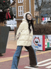 a woman wearing a white jacket and a hooded hat stands in front of a gingerbread house