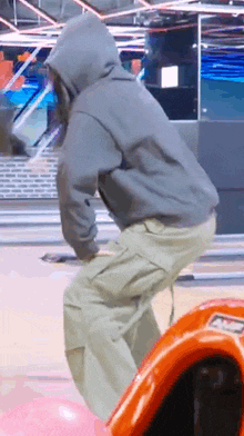a man in a hoodie is riding a bowling alley ball .