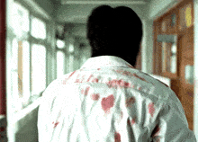 a man in a bloody shirt is walking down a hallway