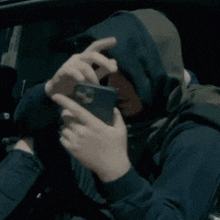 a man wearing a hood is holding a cell phone in front of his face