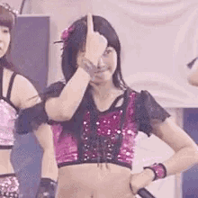 a woman in a pink crop top is making a face with her hand .