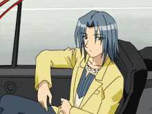 a man with blue hair is sitting in a car with his hand on his knee