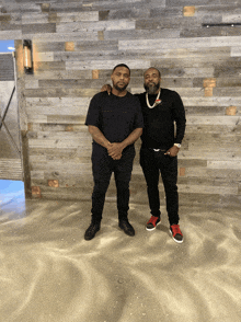 two men standing in front of a wooden wall