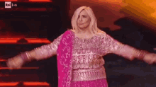 a woman in a pink and silver dress is on a stage with her arms outstretched