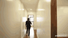 a woman is walking down a hallway with white walls and wooden floors .