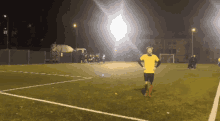 a man in a yellow shirt and black shorts stands on a soccer field at night