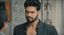 a man with a beard is wearing a black jacket and a black shirt .