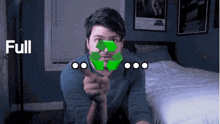 a man is sitting on a bed pointing at the camera with a green recycling symbol in front of his face .