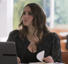 a woman sitting at a desk with a laptop and a piece of paper in her hand
