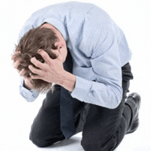 a man in a blue shirt and tie is kneeling down and holding his head