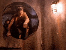 a woman is crawling through a hole in a wall next to a light
