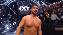 a shirtless wrestler is standing in front of a nxt sign