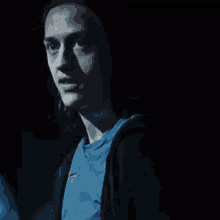 a man wearing a blue shirt and a black jacket is smiling in the dark