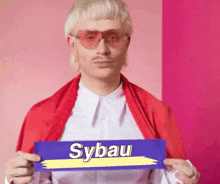 a man wearing sunglasses and a red scarf is holding a sign that says sybau