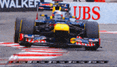 a race car is on a track with a walker ubs banner behind it