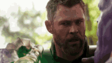 a man with a beard is standing next to a purple statue of thanos .