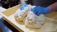 a person wearing blue gloves is kneading dough on a tray that says made in animonica