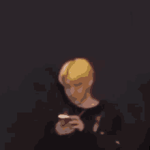 a blurry picture of a man with blonde hair looking at his phone .