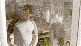 a man in a gray shirt is standing in front of a glass door in a kitchen .