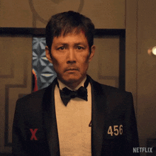 a man in a tuxedo and bow tie has the number 456 on his shirt .
