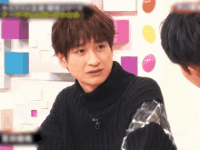 a man wearing a black sweater with a microphone on his neck talks to another man