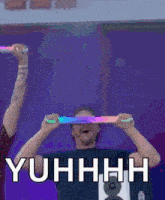 a man is holding glow in the dark sticks in front of his eyes and the words yuhhhh are above him .