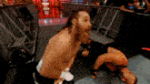 a man with a beard is kneeling down in a wrestling ring with another man laying on the ground .