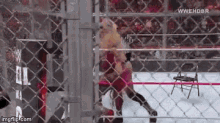 a woman is wrestling in a cage behind a chain link fence .
