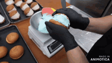 a person wearing black gloves is putting blue frosting on a donut on a scale that says cas