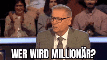 a man in a suit and tie is sitting at a table in front of a crowd and asking , wer wird millionar ?