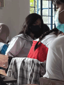 a girl wearing a black face mask sits in a classroom