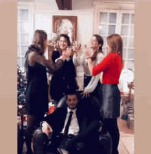 a man in a suit and tie is surrounded by women toasting with champagne
