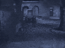 a black and white photo of a group of people walking down a cobblestone street at night .
