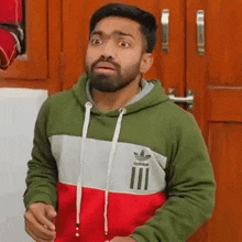 a man with a beard is wearing a green , red and white hoodie .