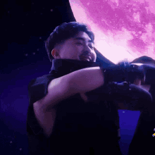 a man in a black shirt stands in front of a purple full moon