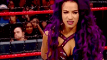 a woman with purple hair is standing in a wrestling ring with a crowd behind her .