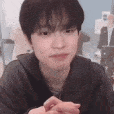 a young man is sitting at a table with his hands folded in front of him .