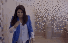 a woman in a blue jacket is walking in a bathroom