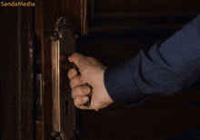 a person 's hand is holding a door knob and the words sandamedia are on the bottom