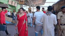 a woman in a red saree is walking in a crowd
